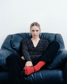 a woman sitting on top of a black chair with red socks in her lap and looking at the camera