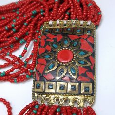 *Description: Bohemian beautiful red Czech seed bead multi-strand tribal fringe necklace with a brass pendant and glass inlay design from the 1970s. The red seed beads have teal blue seed beads scattered throughout the design. The beads are on white thread and have brass end caps. The enamel pendant and fringe are 6 1/2 Inches in length. This would be a great addition to your vintage jewelry collection or make a great vintage gift! *Approximate Measurements: Length - 21 Inches, Pendent Length (w Artisan Red Beads For Festival, Red Bohemian Dangling Beads, Artisan Red Beaded Necklace With Dangling Beads, Red Multi-strand Dangling Beads, Bohemian Red Necklace With Gold Beads, Artisan Multi-strand Red Beads, Red Multi-strand Beads For Festival, Artisan Red Dangling Beads, Bohemian Multi-strand Red Beads