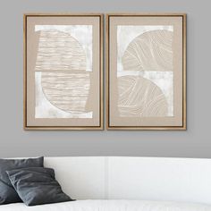 two framed art pieces hang above a white couch