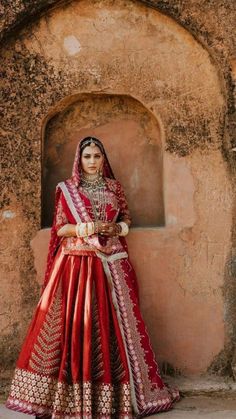 a woman in a red and gold bridal gown standing next to a stone wall