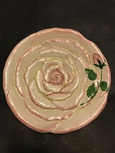 a pink plate with green leaves and a rose on the center is sitting on a black surface