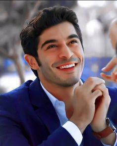 a man in a blue suit smiling and holding his hand to his chin while looking at the camera