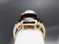 This beautifully structured vintage mounting holds a bold stone! This gem is a gorgeous deep red garnet, weighing in at nearly 10 carats. Garnets are known for their exceptional color and play of light, and this gem is opulent and sophisticated. Metal: 10K Yellow Gold Gem: Garnet 9.88 Carats Gem Measurements: 10.5 x 13.4 mm, Rectangle Cushion Cut Ring Size: 6.25 Marks: "10K" Stamped on the inside band Formal Garnet Ring With Polished Finish, Formal Garnet Burgundy Ring, Formal Burgundy Garnet Ring, Elegant Large Stone Ruby Ring Gift, Elegant Ruby Ring With Large Stone For Gift, Elegant Burgundy Ruby Gemstone Ring, Classic Burgundy Ruby Ring For Formal Occasions, Classic Formal Burgundy Rings, Luxury Gemstones With Large Stone For Formal Events