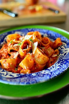 pasta with tomato sauce and parmesan cheese in a blue and green bowl on a wooden table