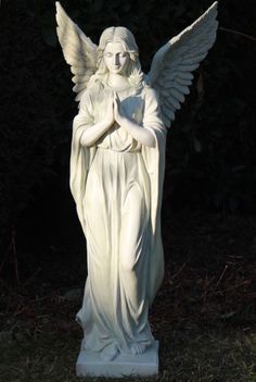 an angel statue in the grass with its arms folded up and hands clasped to her chest