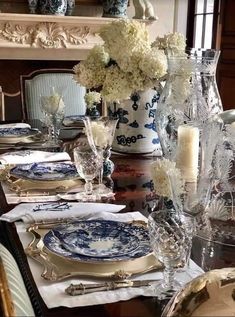 a dining room table is set with blue and white plates, silverware, candles, and flowers