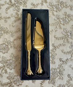 two forks and spoons in a black box on a tablecloth with gold flowers