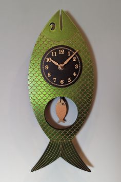 a green fish clock hanging from the side of a wall