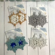 four crocheted earrings are displayed on a white wooden surface with blue and green flowers