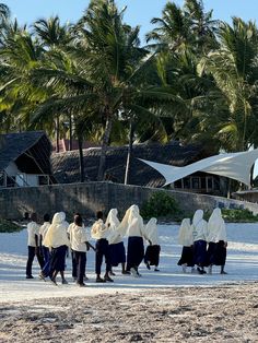 a group of people walking on top of a sandy beach next to palm tree covered buildings