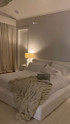 a laptop computer sitting on top of a white bed in a room with beige curtains