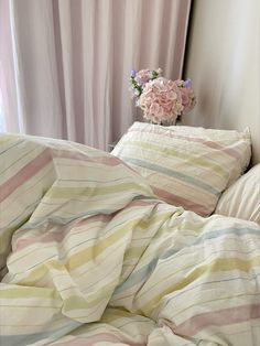 an unmade bed with striped sheets and pink flowers on the nightstand next to it