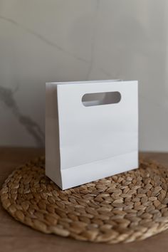 a white paper bag sitting on top of a woven place mat next to a vase