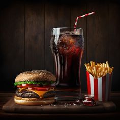 a hamburger, fries and soda on a wooden table next to a glass with cola