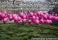 a bunch of pink balloons floating in the air on top of a grass covered field