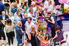 a group of people standing around a table with food and drinks on it in a crowded room