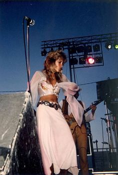 a woman in a white dress standing next to a man with a guitar on stage