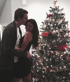 a man and woman kissing in front of a christmas tree