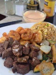 a white plate topped with meat and veggies next to rice on a table