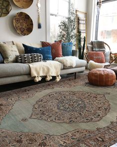 a living room filled with lots of furniture and pillows on top of a rug in front of a window