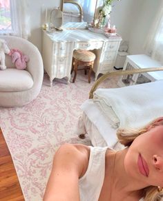 a woman laying on top of a bed next to a white chair and desk in a bedroom