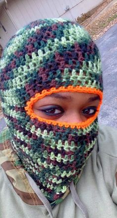 a young boy wearing a crocheted green and brown hat with an orange eye patch