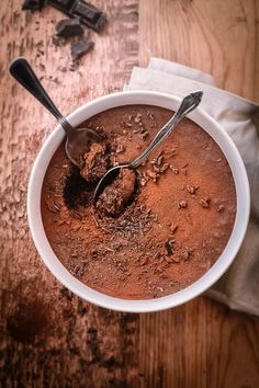 a white bowl filled with chocolate on top of a wooden table next to two spoons