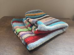 two multicolored knitted blankets sitting on top of a wooden table next to a wall