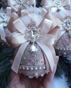 a hand is holding some ornaments with bows and pearls on them in front of pine branches