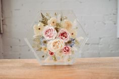 a clear vase filled with flowers sitting on top of a wooden table next to a white brick wall