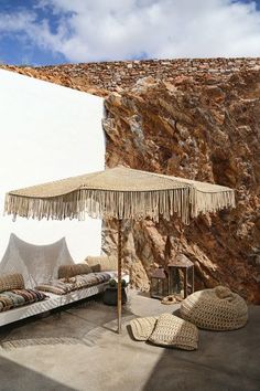 an outdoor seating area with pillows and umbrellas on the ground next to a rock wall