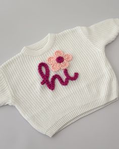 a white sweater with a pink flower on the front and an embroidered monogram in the middle