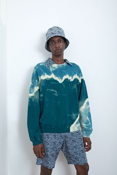 a man standing in front of a white wall wearing a blue tie - dyed sweatshirt and shorts