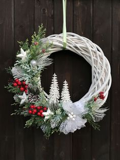 a white wreath hanging on a wooden fence with evergreens, berries and pine cones