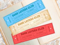 two book lover's club tickets sitting on top of an open book next to each other