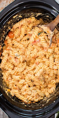 a wooden spoon in a black crock pot filled with macaroni and cheese