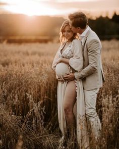 a pregnant couple cuddles in a field as the sun goes down on them