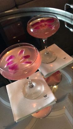 two martinis with pink flowers in them on top of a glass table at a restaurant