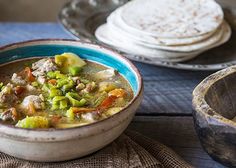 there is a bowl of soup on the table with tortillas in the background