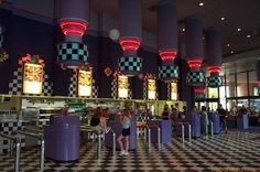 people are sitting at the checkered floor in front of some food court booths with lights on them