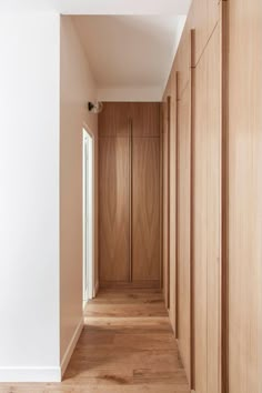 an empty hallway with wooden cabinets and white walls, leading to another room that has light wood flooring