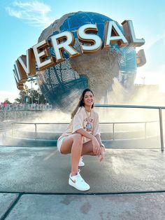 a woman sitting on the ground in front of a sign that says universal with a blue globe behind her