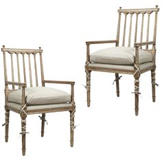 two wooden chairs with beige cushions and white linen on them, one is turned to the side