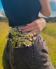 a woman is holding flowers in her jeans pocket