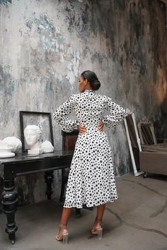 a woman in a white and black dress standing next to a table with a mirror on it