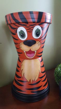 an orange and black tiger pot sitting on top of a wooden table next to a plant