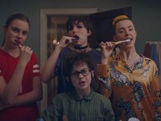 three women brushing their teeth in front of a mirror while another woman brushes her teeth