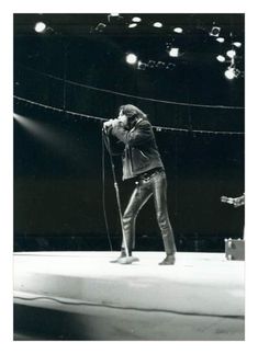 two men on stage with microphones in their hands and one man holding something up to his ear