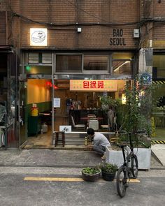 a man sitting on the sidewalk in front of a building with plants growing out of it