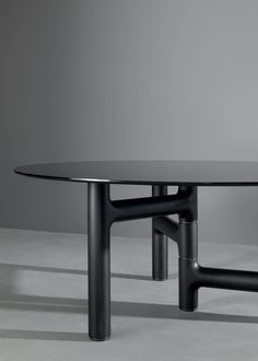 an oval glass table with two black metal legs on the top and bottom, against a gray background